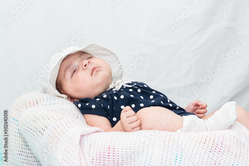 beautiful caucasian baby sleeping peacefully on a small cradle, dressed in a blue smock and a white hat. on a white background with space to copy text. photo