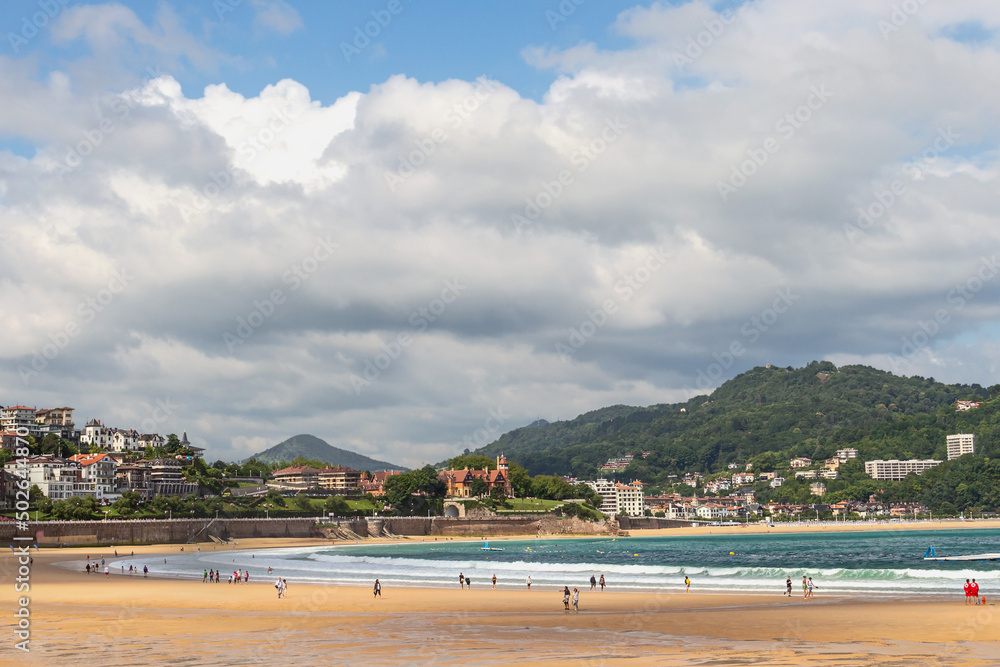 Wide sandy beach with people walking on a sunny day on the ocean coast in the Spanish city of San Sebastian