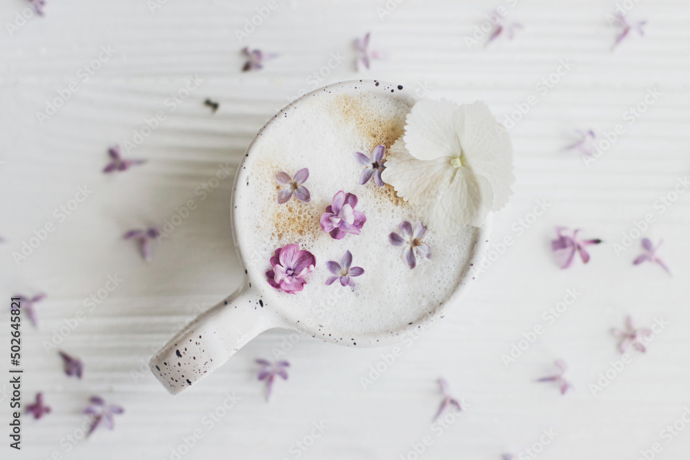 Delicious coffee with lilac petals on white wooden background flat lay. Happy mothers day. Good morning, welcoming spring. Beautiful flowers in stylish cup of coffee still life. Delicious coffee with lilac petals on white wooden background flat lay. Happy mothers day. Good morning, welcoming spring. Beautiful flowers in stylish cup of coffee still life.