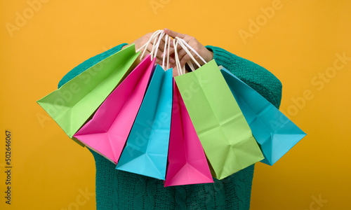 a woman in a sweater holds a paper bag on a yellow background and shows a like gesture with her hand. Purchases. Seasonal sale
