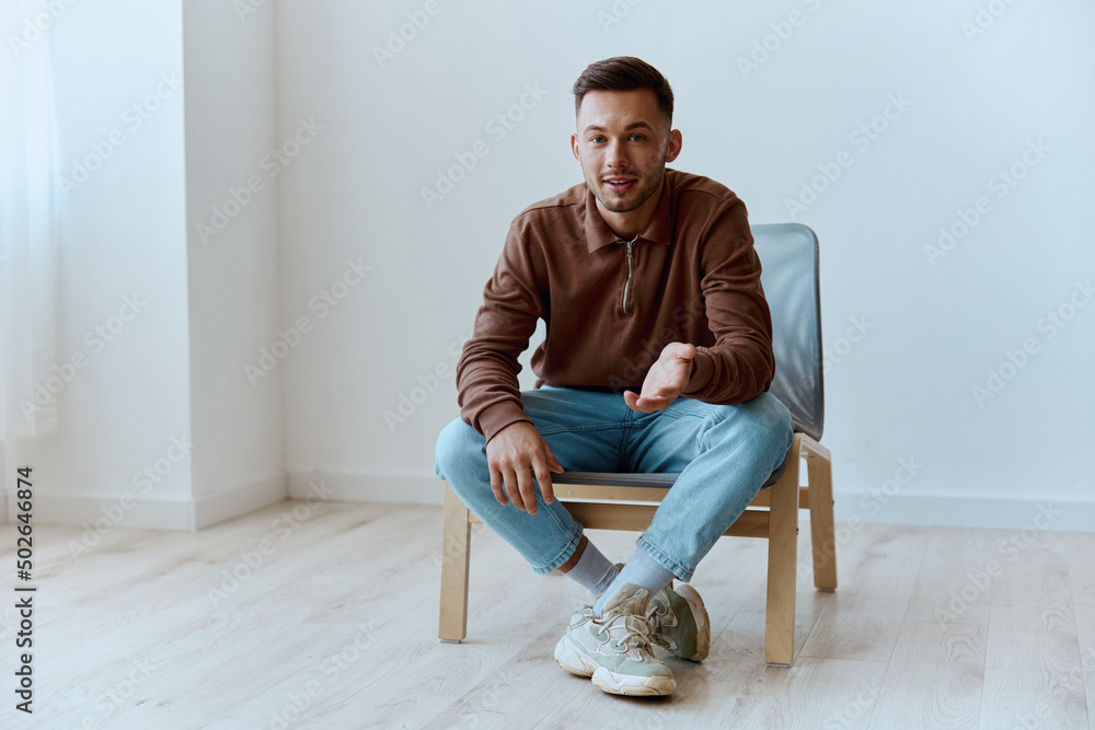 Cheerful cute happy young tanned man guy smiling point hand at camera say Hey Welcome sitting in chair at home. Distance communication Gadget using concept. Copy space for ad