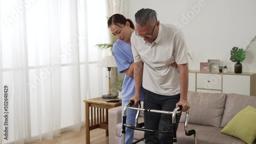 slow motion of asian senior stroke patient undergoing rehab exercise with a walker at home. the woman nursing aide assists him during home visit