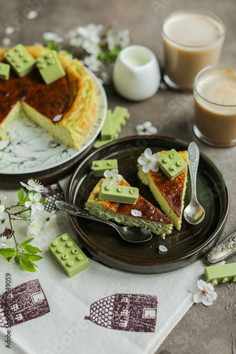 Cheesecake with matcha decorated with designer chocolate. Grilled San Sebastian cheesecake with green tea on a table with coffee and spring flowers.