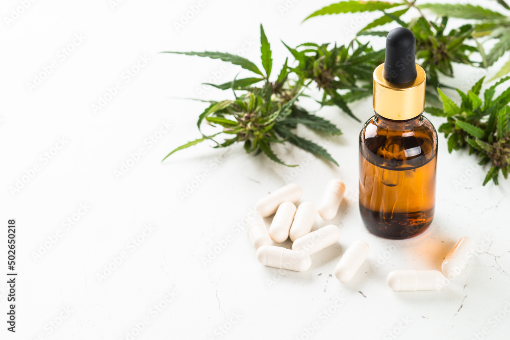 Fototapeta premium CBD pills and CBD oil in glass bottle at white table. Cannabis medicine. Sedative, antibiotic, antioxidant using.