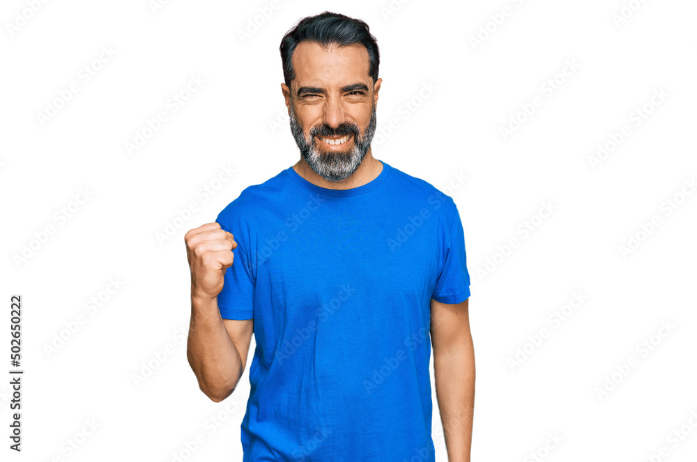 Middle aged man with beard wearing casual blue t shirt angry and mad raising fist frustrated and furious while shouting with anger. rage and aggressive concept. Middle aged man with beard wearing casual blue t shirt angry and mad raising fist frustrated and furious while shouting with anger. rage and aggressive concept.