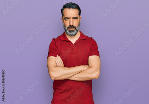 Middle aged man with beard wearing casual red t shirt skeptic and nervous, disapproving expression on face with crossed arms. negative person.
