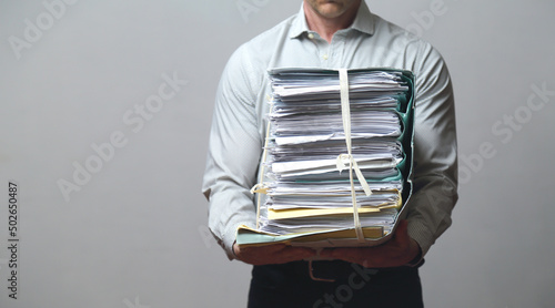 Impiegato con fatica tiene tra le braccia un enorme fascicolo di documenti photo