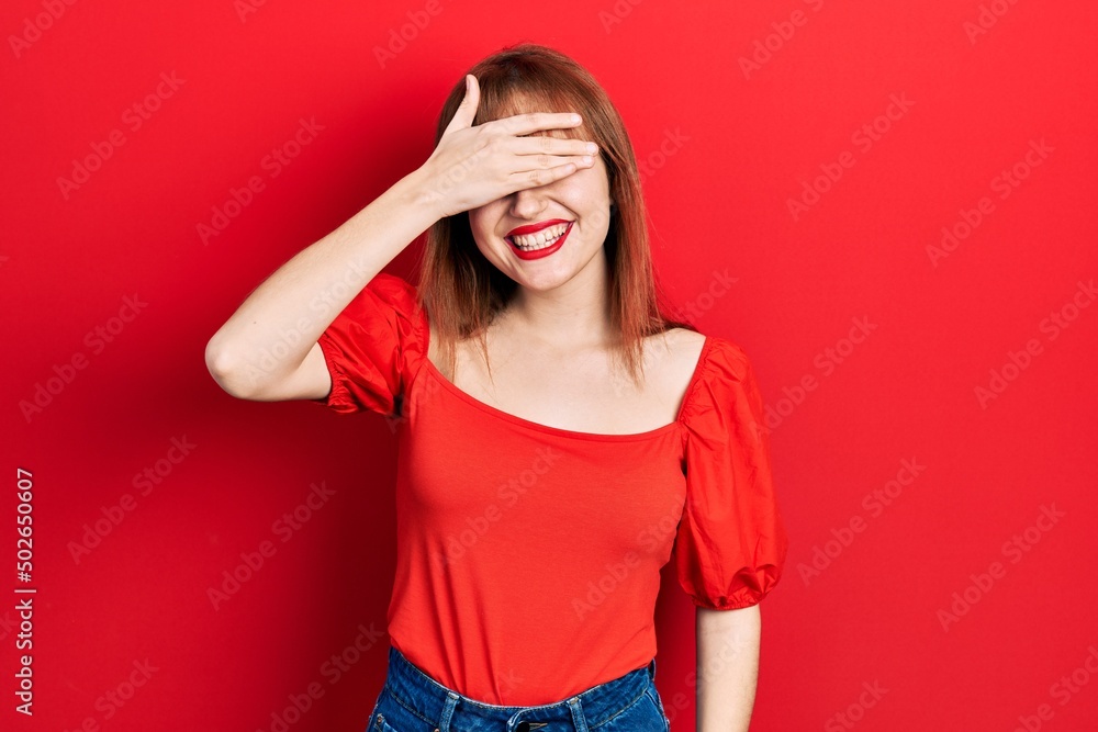 Redhead young woman wearing casual red t shirt smiling and laughing with hand on face covering eyes for surprise. blind concept. Redhead young woman wearing casual red t shirt smiling and laughing with hand on face covering eyes for surprise. blind concept.