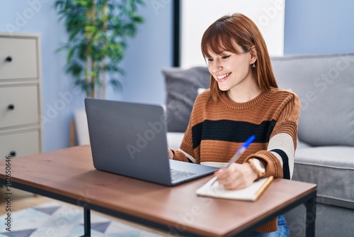 Young woman using laptop writing on notebook at home