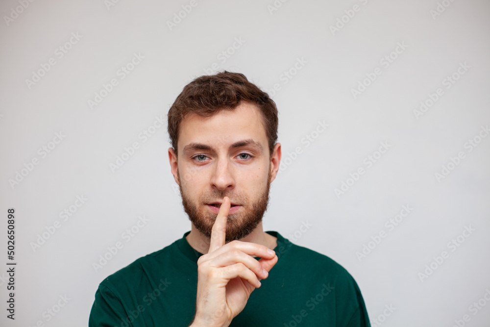 a young man covers his mouth with his finger, silence, do not talk a young man covers his mouth with his finger, silence, do not talk