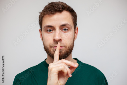 a young man covers his mouth with his finger, silence, do not talk