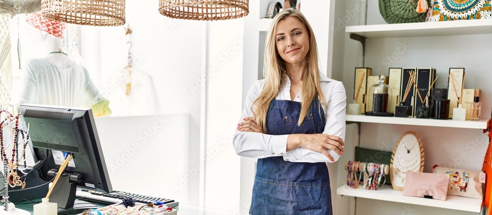Young caucasian shopkeeper woman smiling happy standing with arms crossed gesture at clothing store. Young caucasian shopkeeper woman smiling happy standing with arms crossed gesture at clothing store.