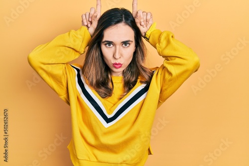 Young hispanic girl wearing casual clothes doing funny gesture with finger over head as bull horns
