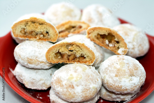 Red plate of traditional Arabic cookies for celebration of Islamic holidays of El-Fitr feast, Egyptian Kahk covered with powdered sugar and stuffed nuts and hazelnuts and Malban isolated on white photo