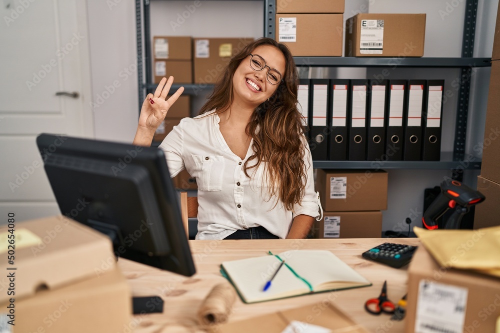 Young hispanic woman working at small business ecommerce showing and pointing up with fingers number three while smiling confident and happy. Young hispanic woman working at small business ecommerce showing and pointing up with fingers number three while smiling confident and happy.