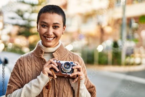 Beautiful hispanic woman with short hair smiling happy outdoors holding vintage camera