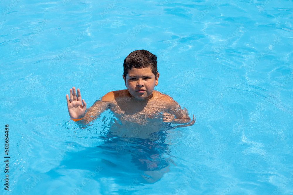 child in swimming pool with one hand open and the other closed, summer vacation