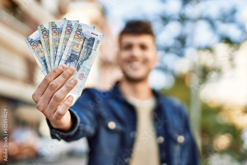 Young hispanic man smiling happy holding peruvian sol banknotes at the city photo