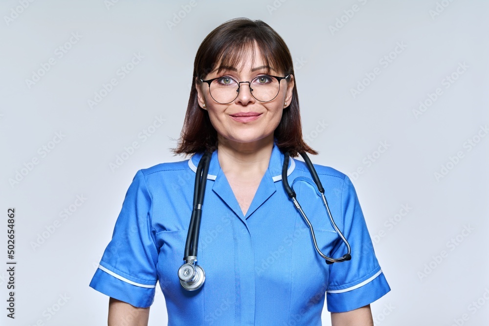 Headshot portrait of nurse in blue uniform looking at camera on light studio background Headshot portrait of nurse in blue uniform looking at camera on light studio background