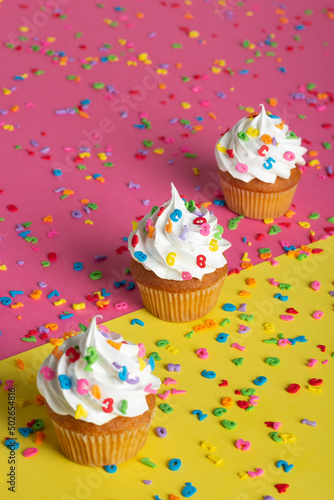 Close-up view of cupcakes adorned with whipped cream and sprinkles  placed on a split-color background.
