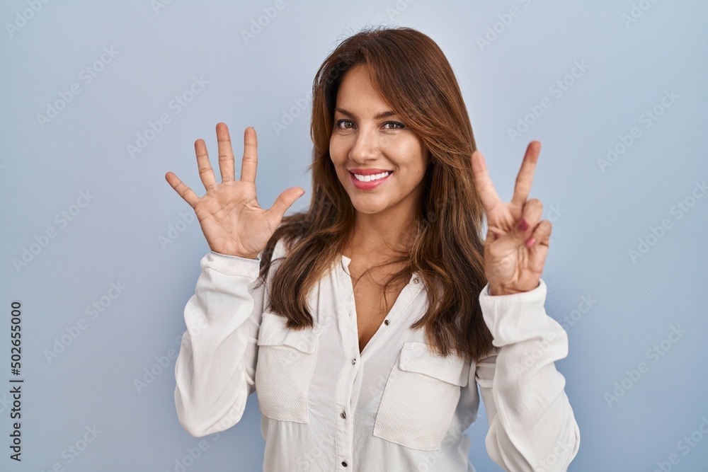Hispanic woman standing over isolated background showing and pointing up with fingers number seven while smiling confident and happy. Hispanic woman standing over isolated background showing and pointing up with fingers number seven while smiling confident and happy.