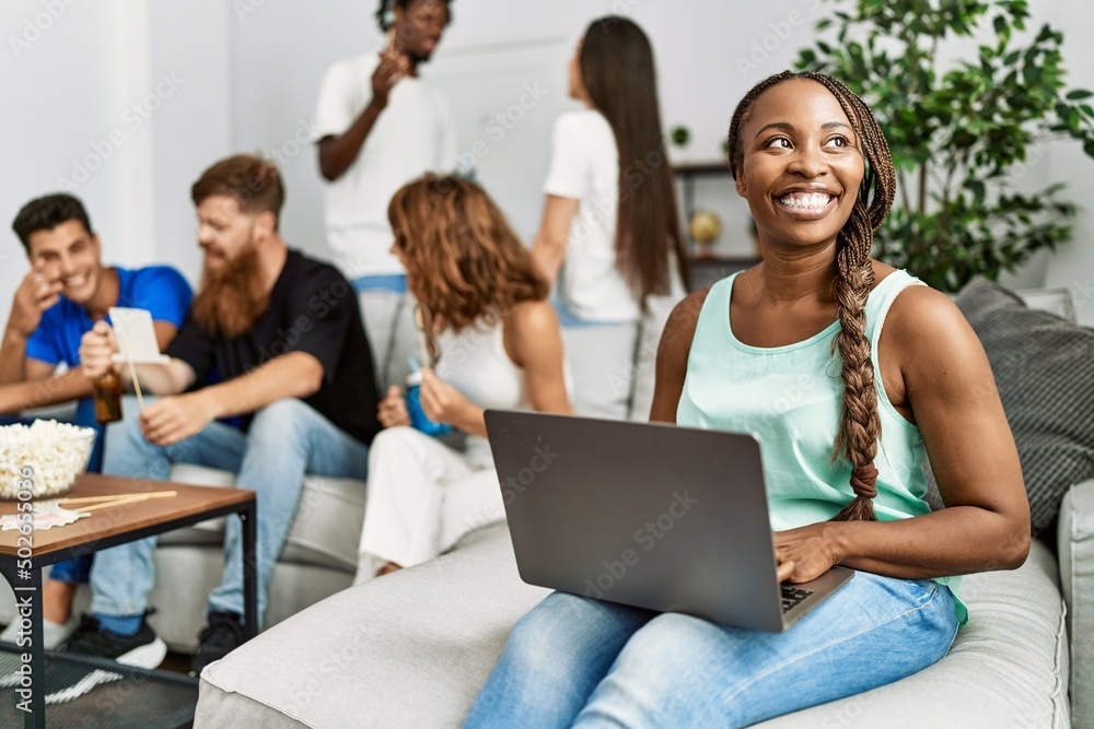 Group of young friends smiling happy sitting on the sofa. Woman using laptop at home. Group of young friends smiling happy sitting on the sofa. Woman using laptop at home.