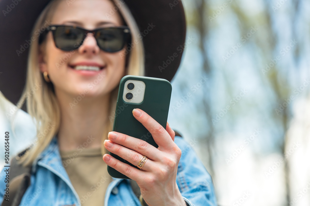 Stylish woman in hat and sunglasses looking in to mobile phone outdoor