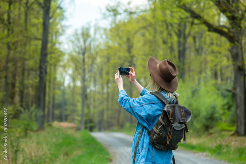 Stylish woman in hat and backpack make a photo with mobile phone outdoor