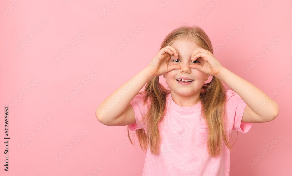 Portrait of cute cheerful playful little girl with ponytails holding hands like glasses or binocular. Isolated over pink background with copy space. Portrait of cute cheerful playful little girl with ponytails holding hands like glasses or binocular. Isolated over pink background with copy space.