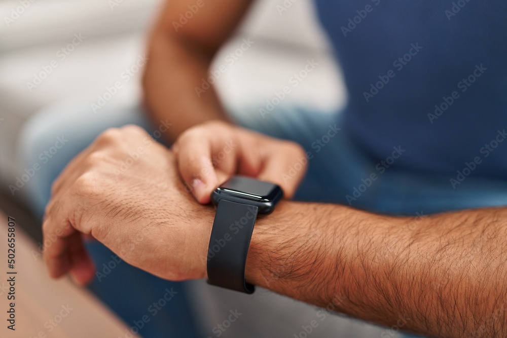 Young hispanic man using smartwatch at home