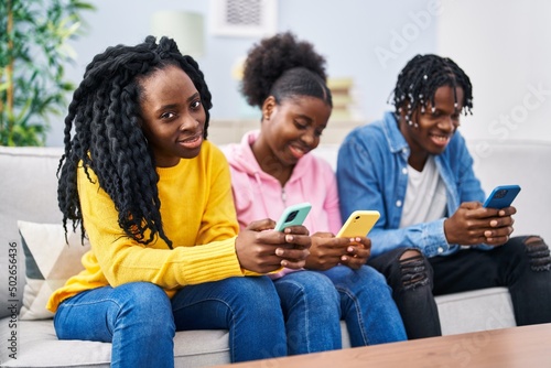 African american friends using smartphone sitting on sofa at home