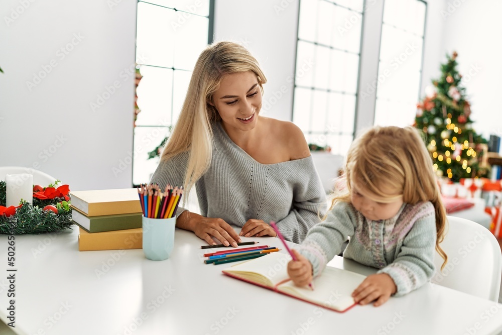Fototapeta premium Mother and daughter drawing on notebook sitting by christmas tree at home