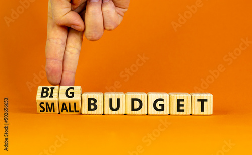 Big or small budget symbol. Businessman turns wooden cubes and changes words Small budget to Big budget. Beautiful orange table orange background, copy space. Business big or small budget concept.