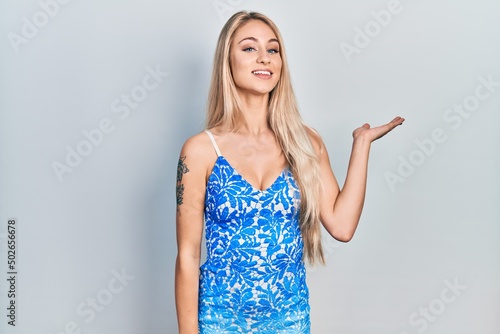 Young beautiful caucasian woman wearing summer dress smiling cheerful presenting and pointing with palm of hand looking at the camera.