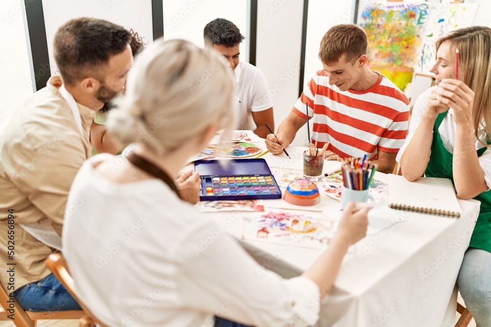 Group of people smiling happy drawing sitting on the table at art studio.