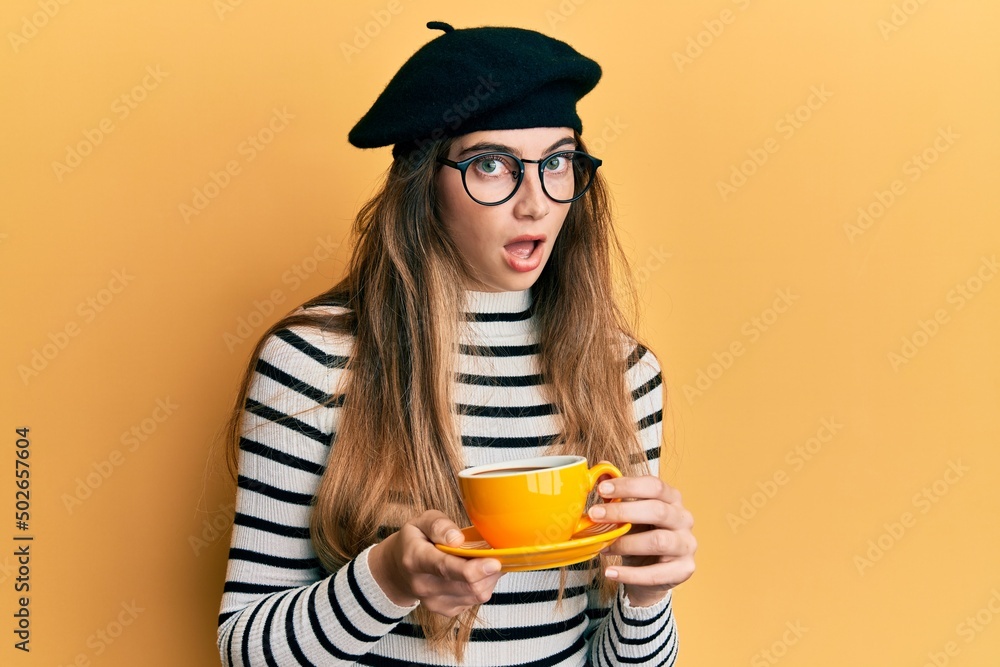 Young caucasian woman wearing french style drinking a cup of coffee afraid and shocked with surprise and amazed expression, fear and excited face. Young caucasian woman wearing french style drinking a cup of coffee afraid and shocked with surprise and amazed expression, fear and excited face.