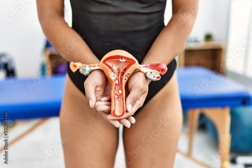 Young african american woman holding anatomical model of fallopian tube at clinic photo