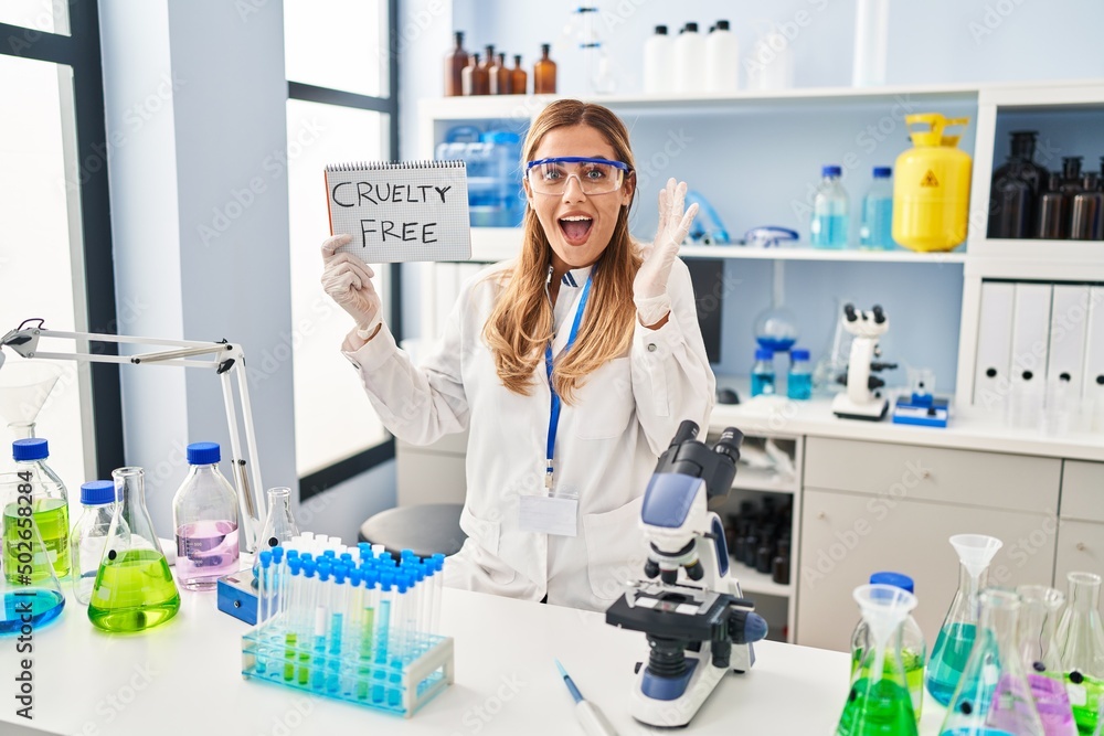 Young blonde scientist woman working on cruelty free laboratory celebrating victory with happy smile and winner expression with raised hands Young blonde scientist woman working on cruelty free laboratory celebrating victory with happy smile and winner expression with raised hands