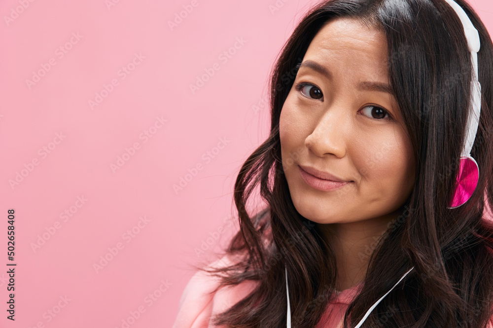 Smiling cutie cute Asian young lady in pink hoodie sweatshirt with cute headphones looks at you with love posing isolated on pink studio background. Good offer. Sound streaming platform ad concept Smiling cutie cute Asian young lady in pink hoodie sweatshirt with cute headphones looks at you with love posing isolated on pink studio background. Good offer. Sound streaming platform ad concept