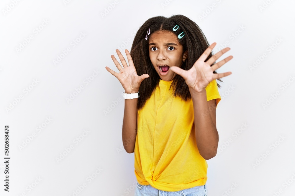 Young african american girl standing over white isolated background afraid and terrified with fear expression stop gesture with hands, shouting in shock. panic concept. Young african american girl standing over white isolated background afraid and terrified with fear expression stop gesture with hands, shouting in shock. panic concept.