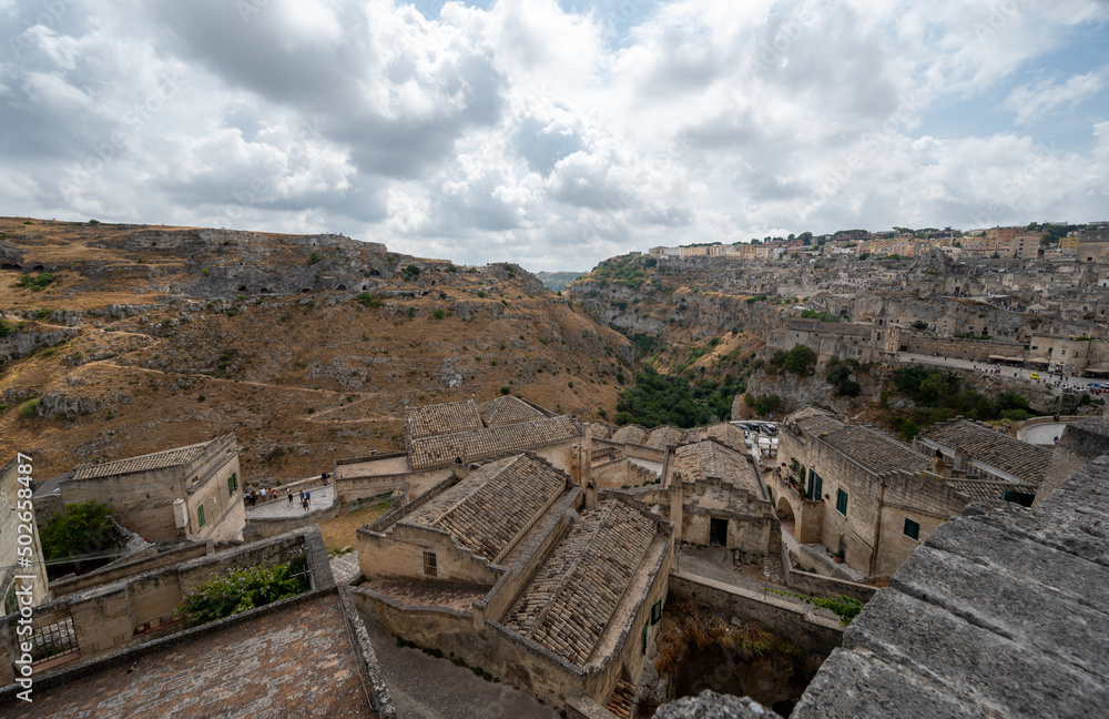 Matera, Basilicata, Italy. August 2021. Splendid daytime panoramic view of the stones of Matera. On the hill on the left the ancient caves are recognizable. On the right the old dark stone houses.