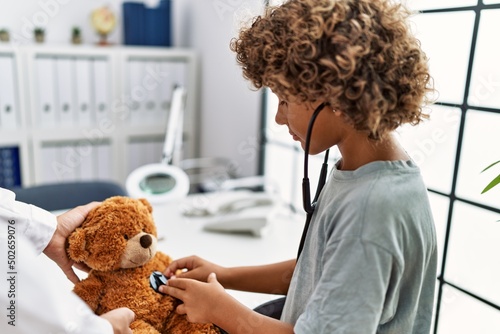 Mother and son wearing doctor uniform auscultating teddy bear at clinic