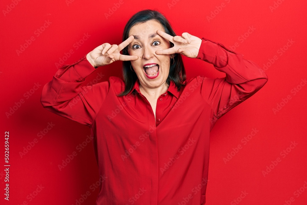 Middle age hispanic woman wearing casual clothes doing peace symbol with fingers over face, smiling cheerful showing victory Middle age hispanic woman wearing casual clothes doing peace symbol with fingers over face, smiling cheerful showing victory