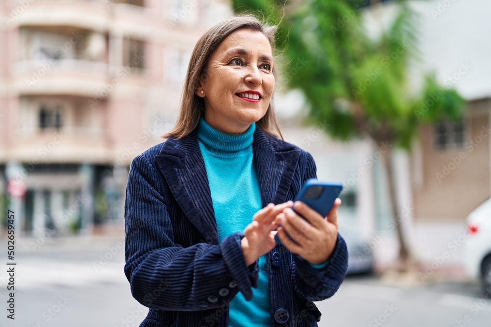 Fototapeta premium Middle age woman business executive using smartphone at street