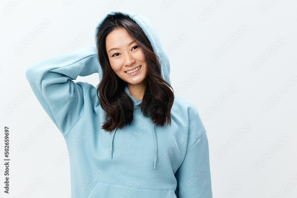 Fashionable smiling happy cute Asian young female in blue sweatshirt puts on the hood posing isolated on over white studio background. The best offer for ad. Fashion New Collection Ad concept Fashionable smiling happy cute Asian young female in blue sweatshirt puts on the hood posing isolated on over white studio background. The best offer for ad. Fashion New Collection Ad concept