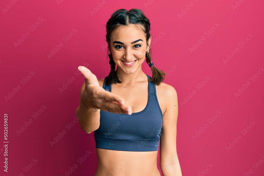 Young brunette girl wearing sportswear and braids smiling friendly offering handshake as greeting and welcoming. successful business.