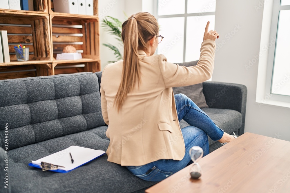 Young woman working at consultation office posing backwards pointing ahead with finger hand Young woman working at consultation office posing backwards pointing ahead with finger hand