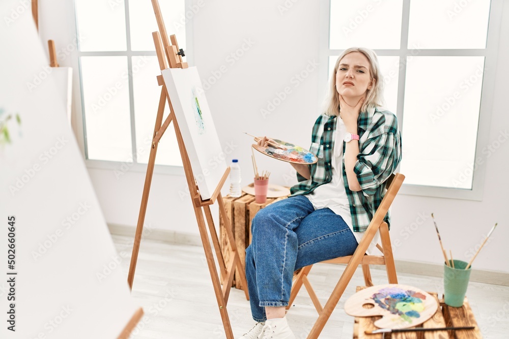Young artist woman painting on canvas at art studio touching painful neck, sore throat for flu, clod and infection