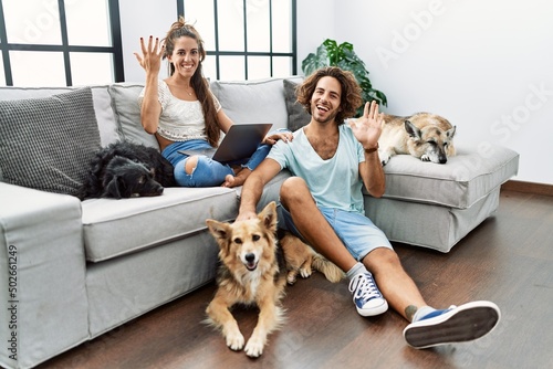 Photography Young hispanic couple with dogs relaxing at home waiving saying hello happy and