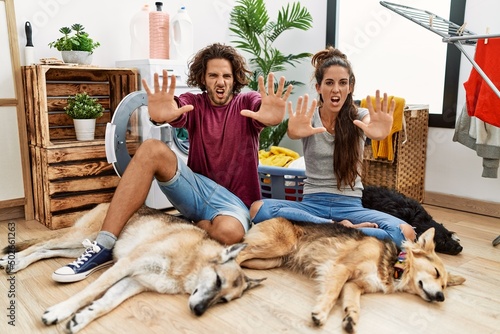 Young hispanic couple doing laundry with dogs doing stop gesture with hands palms  angry and frustration expression